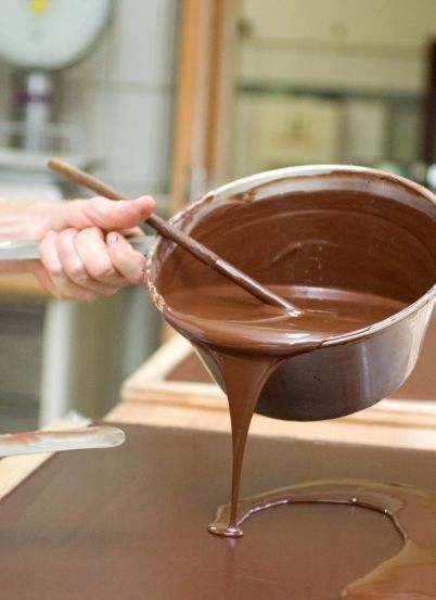 Eine Person gießt Schokolade aus einer Schüssel auf einen Holztisch.