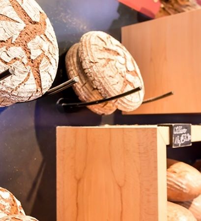 Eine Bäckerei-Auslage zeigt verschiedene Brotsorten, einschließlich ganzer Brote und geschnittenes Brot, auf Holzregalen angeordnet.