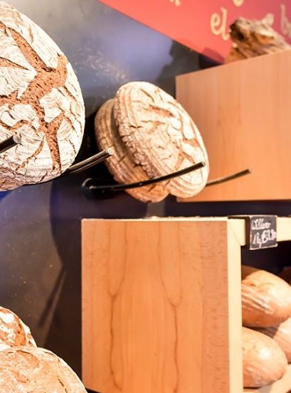 Eine Bäckerei-Auslage zeigt verschiedene Brotsorten, einschließlich ganzer Brote und geschnittenes Brot, auf Holzregalen angeordnet.