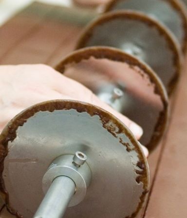 Nahaufnahme einer Hand, die eine Metallscheibe mit Schokoladenüberzug hält. Die Scheibe ist Teil einer Maschine, die mit Schokolade überzogene Kekse herstellt.