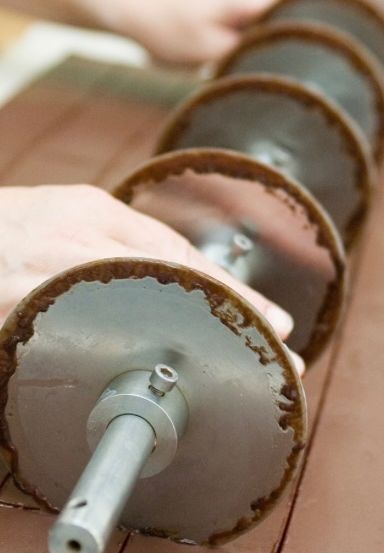 Nahaufnahme einer Hand, die eine Metallscheibe mit Schokoladenüberzug hält. Die Scheibe ist Teil einer Maschine, die mit Schokolade überzogene Kekse herstellt.