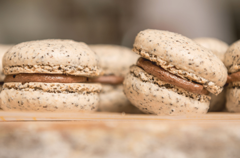 Several macarons are placed on a wooden surface. They have a creamy filling in the middle and a slightly grainy texture on the outside.