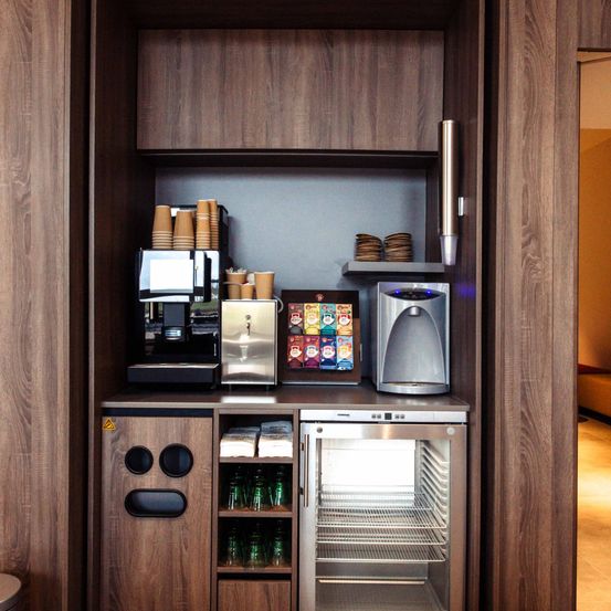 Eine kleine Küchenzeile in einem Hotelzimmer mit einer Kaffeemaschine, einem kleinen Kühlschrank und einem kleinen Rahmen auf dem Tresen.