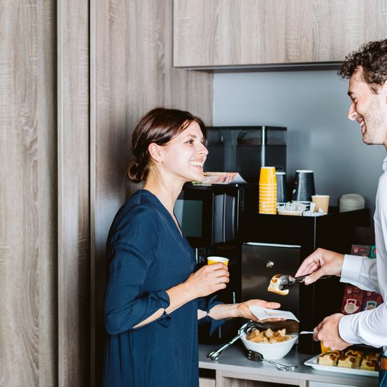Ein Mann und eine Frau teilen sich eine Mahlzeit in der Küche. Der Mann serviert Essen aus einer Schüssel der Frau, die einen Becher hält.