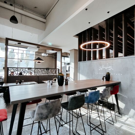 Ein modernes Innendesign eines Cafés mit einem großen Tisch und Barhockern. Eine kreisförmige Leuchte hängt von der Decke.