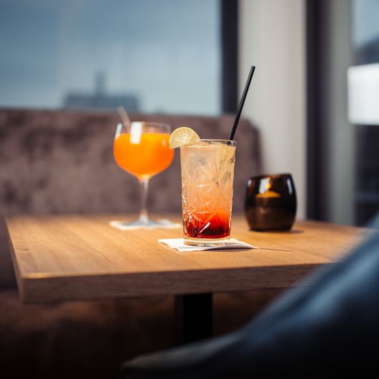 Zwei Gläser mit Cocktails und Strohhalmen und einer Zitrone auf einem Tisch in einem Restaurant.