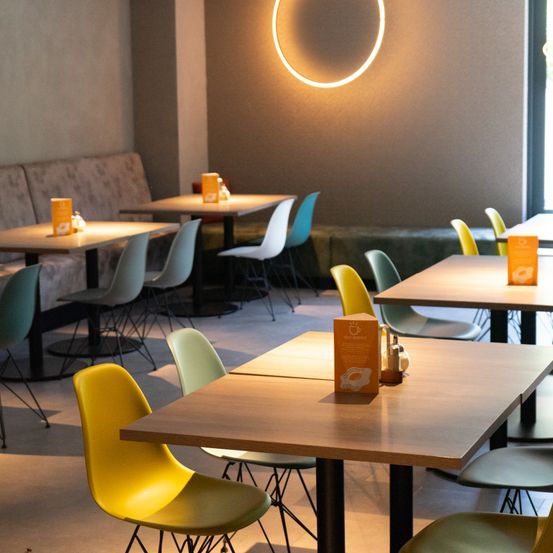 Ein leerer Essraum mit kreisförmigen Lichtern und farbigen Stühlen. Jeder Tisch hat einen Eierkarton. Die Stühle sind in verschiedenen Farben.