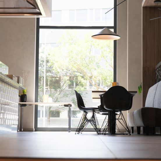 Ein Innenbereich für Mahlzeiten mit modernem Design. Ein Tisch mit vier Stühlen steht in der Nähe des Fensters, das eine Aussicht auf Bäume und Gebäude zeigt.