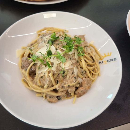 Ein Teller mit Nudeln in cremiger Pilzsauce, mit Käse und Kräutern garniert, auf einem weißen Teller serviert.