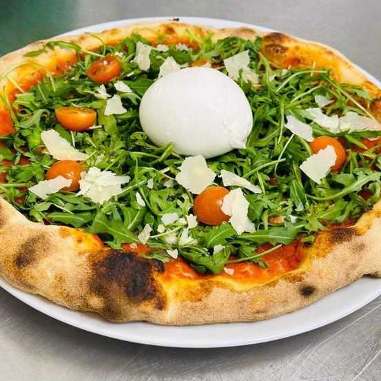 Eine Pizza mit Rucola, Kirschtomaten und einer Burrata-Käsekugel auf einem weißen Teller.