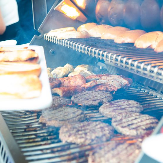 Ein Grill mit verschiedenen Fleischsorten und Brötchen, einschließlich Hamburger, Würstchen und Brötchen, mit einer Tablett Brot links.