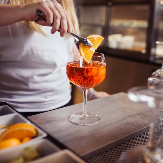 Eine Frau fügt einem Cocktail in einem hohen Glas auf einer Arbeitsplatte eine Orangenscheibe hinzu.