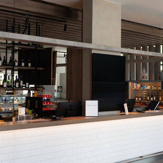 Eine moderne Bartheken mit Monitoren, einer Anzeige und Regalen voller Weinflaschen. Die Theke hat eine weiße geflieste Vorderseite und eine braune Holzrückseite mit einem großen schwarzen Bildschirm an der Wand.