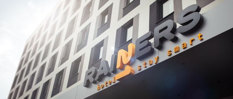Die Vorderseite eines modernen Hotels mit dem Namen Rainers. Das Hotel hat viele Fenster und ein Schild mit dem Text smart stay.
