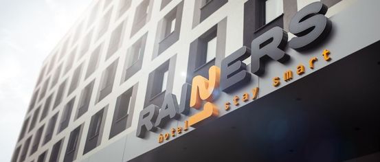 Die Vorderseite eines modernen Hotels mit dem Namen Rainers. Das Hotel hat viele Fenster und ein Schild mit dem Text smart stay.