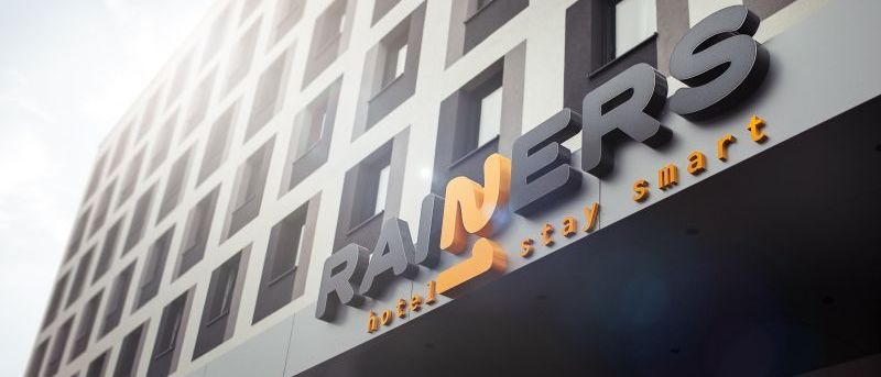 Die Vorderseite eines modernen Hotels mit dem Namen Rainers. Das Hotel hat viele Fenster und ein Schild mit dem Text smart stay.