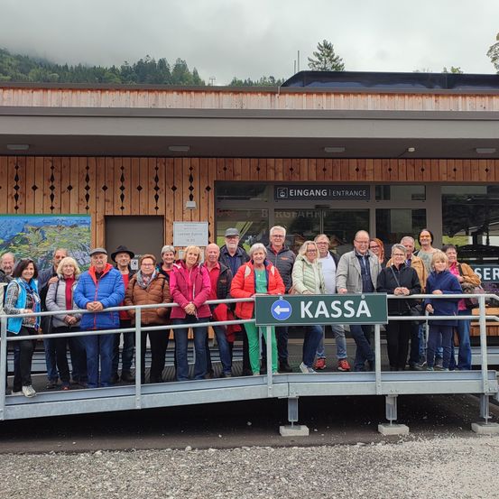 Eine Gruppe von Menschen, wahrscheinlich Touristen, steht vor einem Gebäude mit einem Schild, das auf Kassa zeigt. Sie sind warm gekleidet, was auf kühles Wetter hinweist.