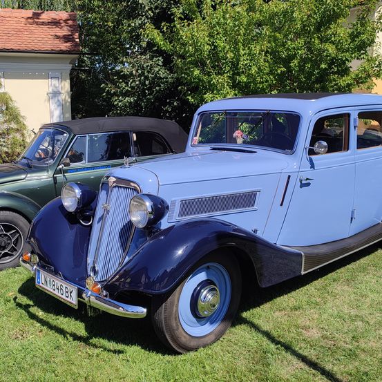Ein klassisches blaues Auto mit dem Kennzeichen LN 846 BK steht auf einem Rasen vor einem Haus mit rotem Dach.