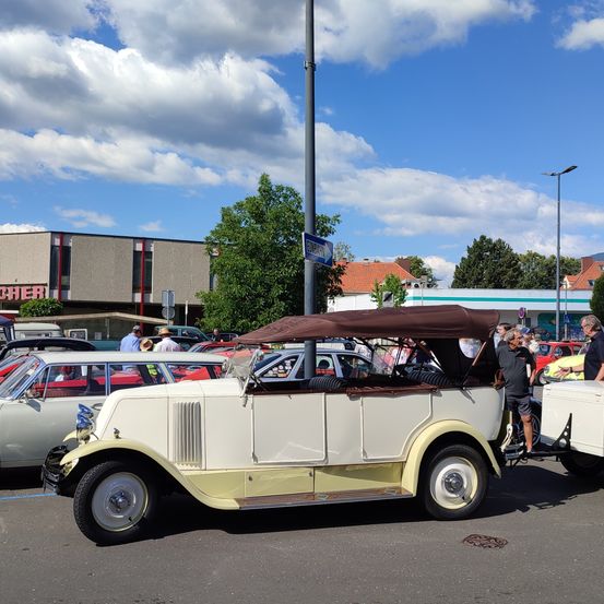 Ein Oldtimer ist auf einem Parkplatz mit anderen Autos geparkt, unter einem blauen Himmel mit Wolken.