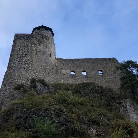 Eine Steinburg mit Turm steht auf einem felsigen Hügel unter blauem Himmel.