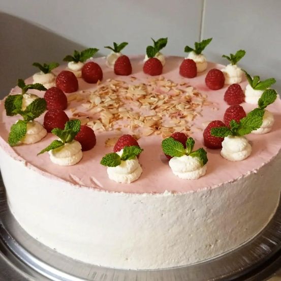 Ein runder Kuchen mit weißer Creme und rosa Himbeerfüllung, garniert mit frischen Himbeeren, Schlagsahne und Minzblättern.
