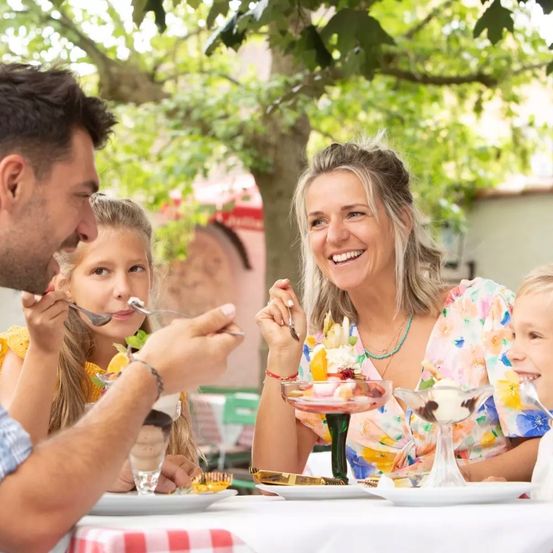 A family enjoys a meal together at an outdoor restaurant, with the man and two girls smiling and eating dessert.