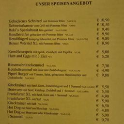 Ein Menü mit verschiedenen Speisen, einschließlich gegrillter Schweinekoteletts, Würsten, Burgern und Hot Dogs, mit ihren jeweiligen Preisen in Euro.