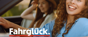Zwei Frauen sitzen in einem Auto, eine lächelt und schaut in die Kamera, die andere hat ihre Hand im Nacken. Das Auto hat das Wort 'Fahrglück' darauf geschrieben.
