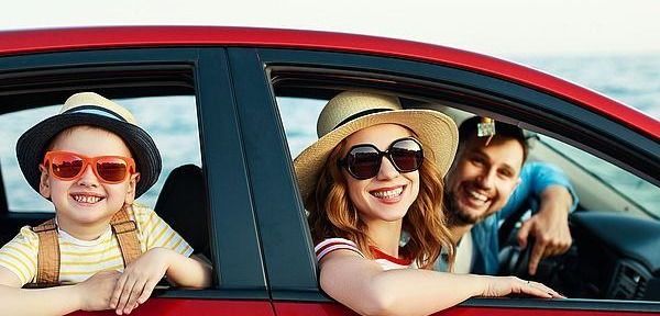 Eine fröhliche Familie in einem roten Auto, alle mit Sonnenbrillen. Der Junge lächelt links, das Mädchen in der Mitte und der Mann fährt rechts. Sie scheinen auf einer Reise zu sein.
