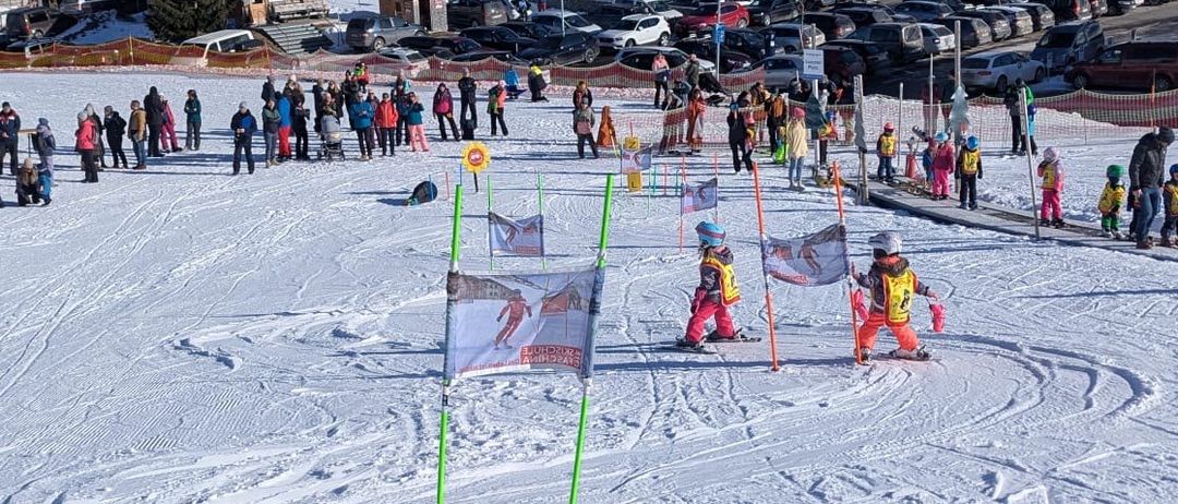 Skifahrer auf einem verschneiten Berg mit einer Skischule. Viele Menschen sind auf den Pisten versammelt, mit Kindern, die in der Nähe von Flaggen Skifahren üben.