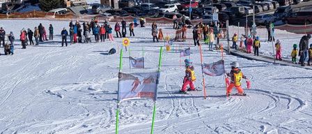 Skifahrer auf einem verschneiten Berg mit einer Skischule. Viele Menschen sind auf den Pisten versammelt, mit Kindern, die in der Nähe von Flaggen Skifahren üben.