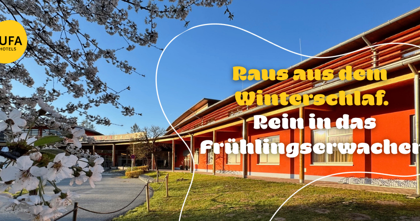 Ein Gebäude im Freien mit Rasenfläche davor und einem blühenden Baum. Ein Text-Overlay sagt 'Raus aus dem Winterschlaf. Rein in das Frühlingserwachen.'