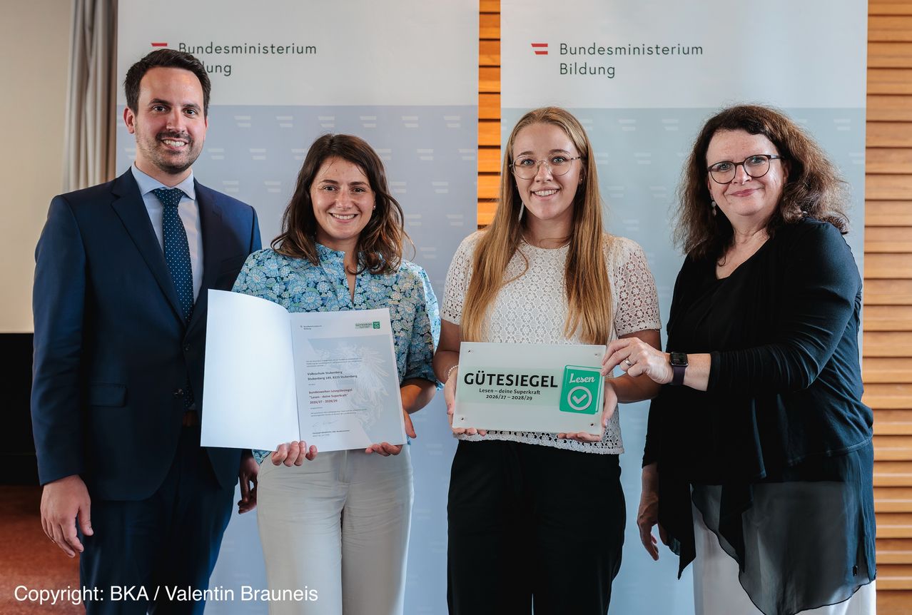 Vier Personen stehen zusammen und halten Urkunden und eine Schachtel mit der Aufschrift 'Gutesiegel'. Zwei Frauen und ein Mann lächeln in die Kamera. Eine Frau auf der rechten Seite trägt eine Uhr.
