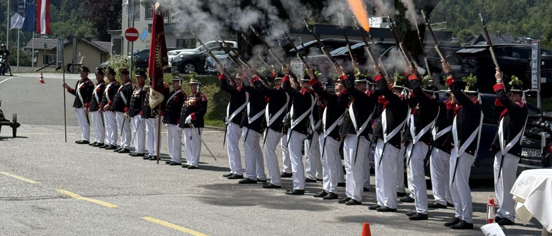 Ein Militärparade mit Soldaten in Uniform, die Gewehre abfeuern und Rauch abgeben auf der Straße.