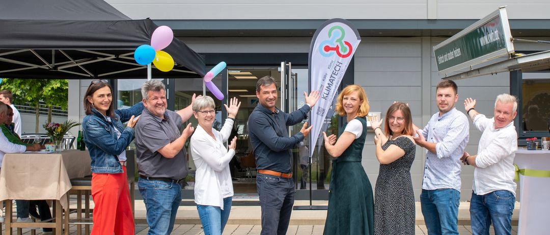 Eine Gruppe von Menschen vor einem Klimatech-Gebäude, feiert mit Luftballons und applaudiert.