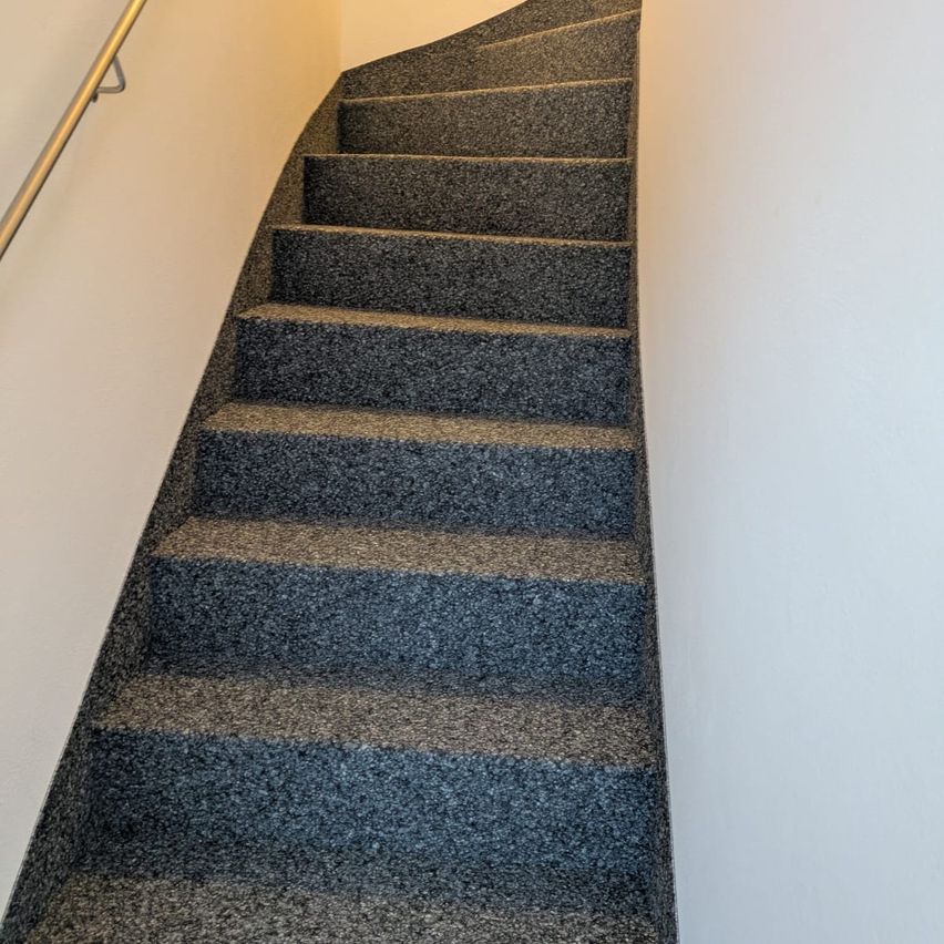 Eine Reihe grauer Betontreppen mit gebogenem Design, einem Metallhandlauf und weißen Wänden.