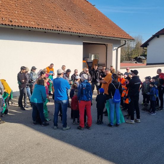 Eine Gruppe von Menschen versammelt sich vor einem Gebäude. Das Gebäude hat ein braunes Dach und die Menschen tragen Jacken, Mützen und Turnschuhe. Sie scheinen auf etwas zu warten und einige schauen auf das Gebäude. Das Gebäude hat eine Glastür und ein Fahrzeug ist im Inneren geparkt.