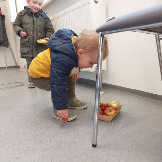 Zwei junge Jungen sind in einem Raum mit Äpfeln und Goldfolie. Ein Junge beugt sich vor, um Essen aufzuheben.