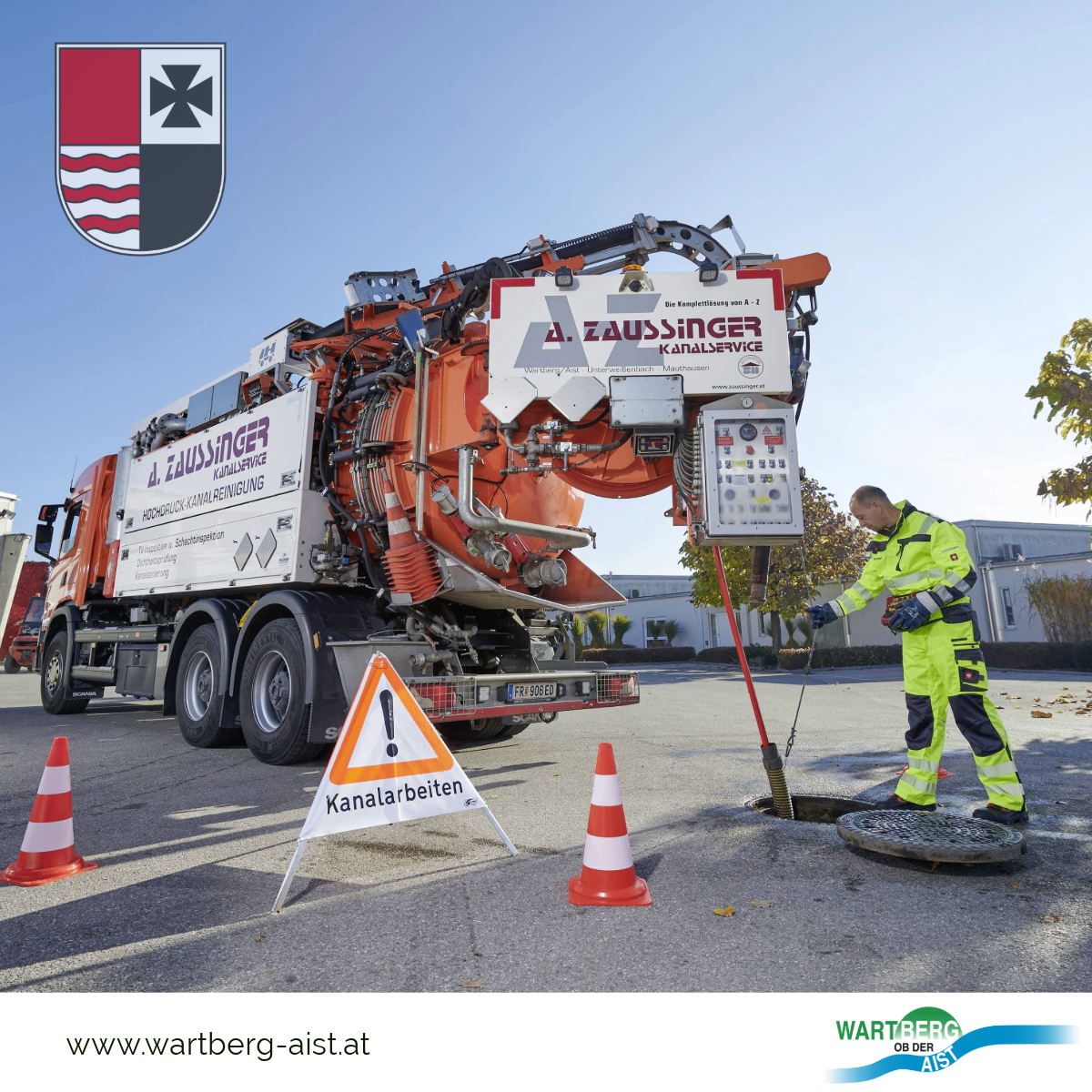 Ein Mann in Schutzkleidung arbeitet mit einem großen orangefarbenen Lastwagen. Es gibt zwei orange-weiße Kegel.