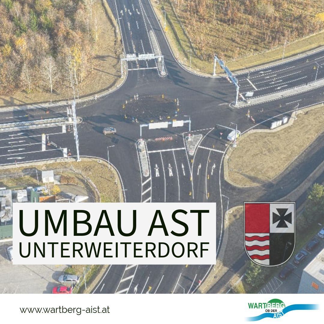 Luftaufnahme einer Baustelle eines Kreisverkehrs mit Fahrzeugen und Absperrungen. Das Schild lautet Umbau AST Unterweiterdorf. Ein Logo mit Kreuz und Streifen ist sichtbar.