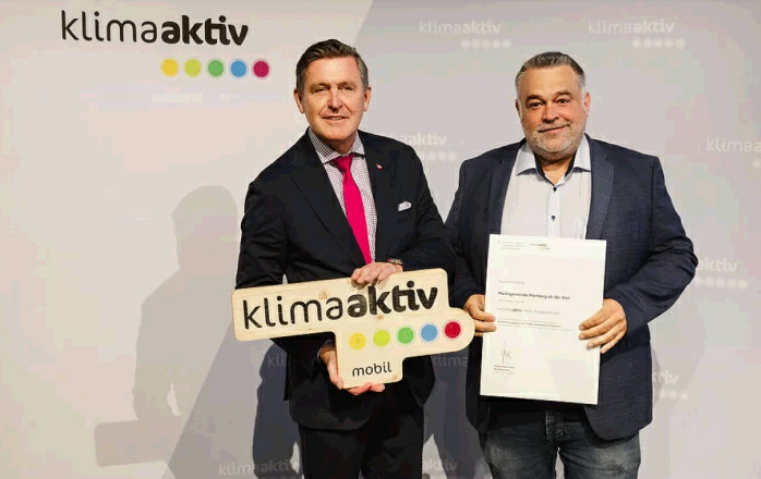 Two men stand in front of a backdrop with the words 'klimaaktiv', holding a sign and a certificate.