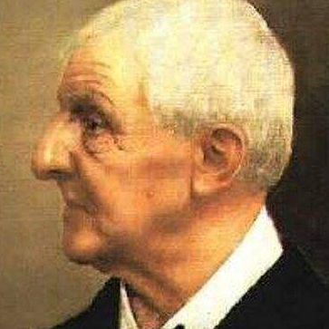 Ein älterer Mann mit weißen Haaren und einem ernsten Gesichtsausdruck. Er trägt einen schwarzen Anzug und ein weißes Hemd.