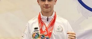 Ein junger Mann in einer weißen Jacke hält drei Medaillen, zwei goldene und eine silberne, und posiert für ein Foto.