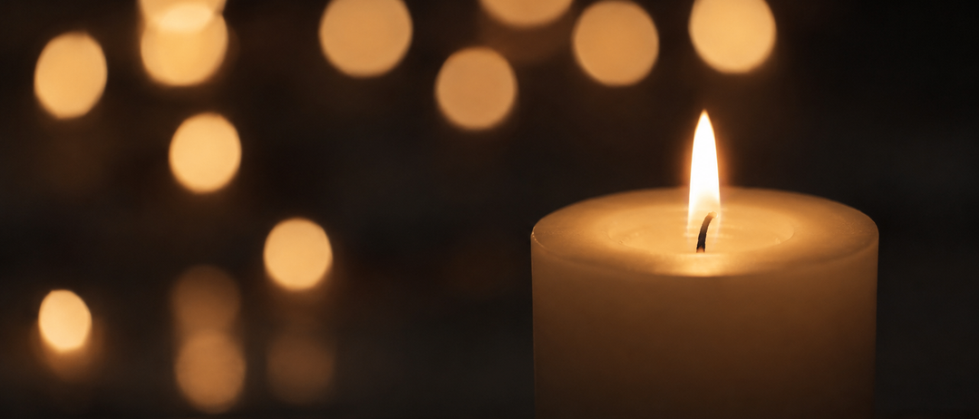 A lit candle stands in the foreground, with several blurred lights in the background, creating a warm, glowing effect.