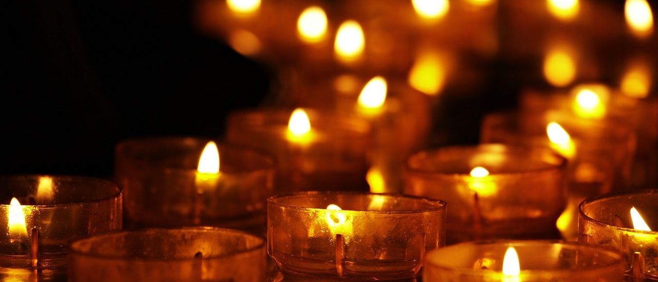 Eine Sammlung von Kerzen, die leuchten und ein warmes Licht in einem schwach beleuchteten Raum verbreiten. Jede Flamme flackert sanft und erhellt die Umgebung.