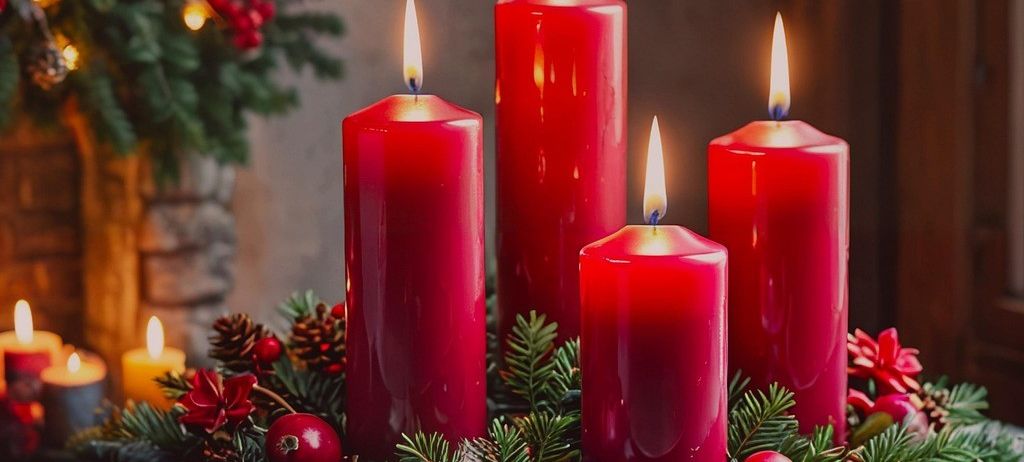 Vier rote Kerzen sind in einer kreisförmigen Anordnung beleuchtet, umgeben von Tannenzapfen, roten Beeren und grünen Blättern, auf einem Holztisch mit einem Weihnachtsbaum im Hintergrund.