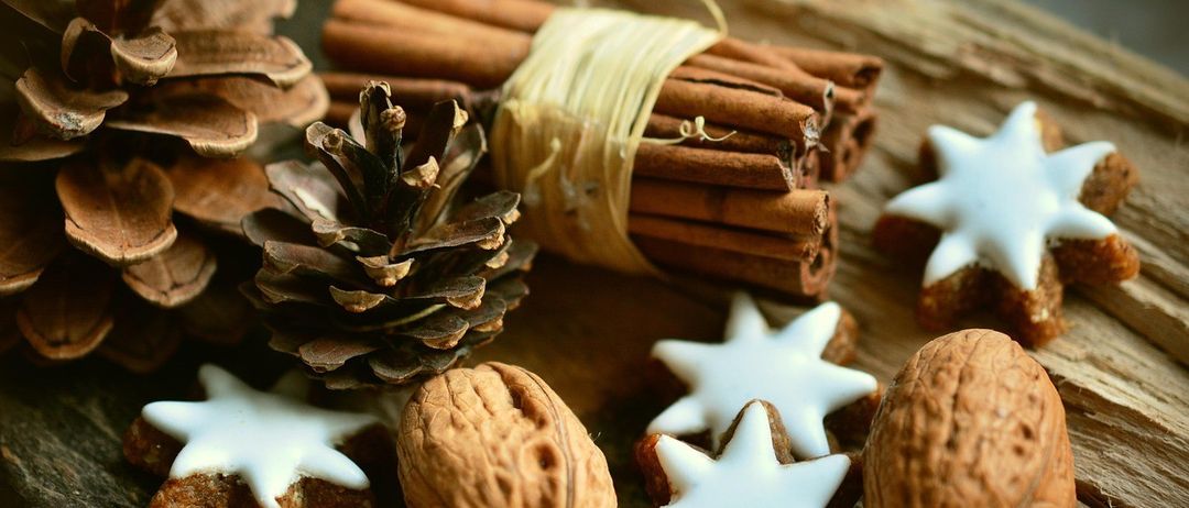 Ein Nahaufnahme von festlichen Gegenständen auf einem Holztisch, einschließlich sternförmiger Kekse, Zimtstangen, einer Walnuss und Tannenzapfen.