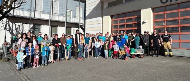 Eine Gruppe von Menschen posiert für ein Foto vor einem Gebäude mit dem Wort ORTS. Sie halten Stöcke und einige haben Trolleys.