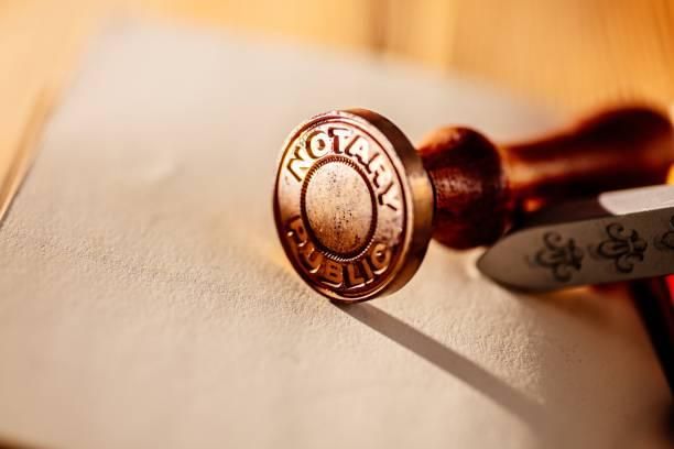 Ein metallischer Notar-Siegelstempel mit der Aufschrift 'NOTARY PUBLIC', auf einem Stück Papier platziert, neben einem Messer.