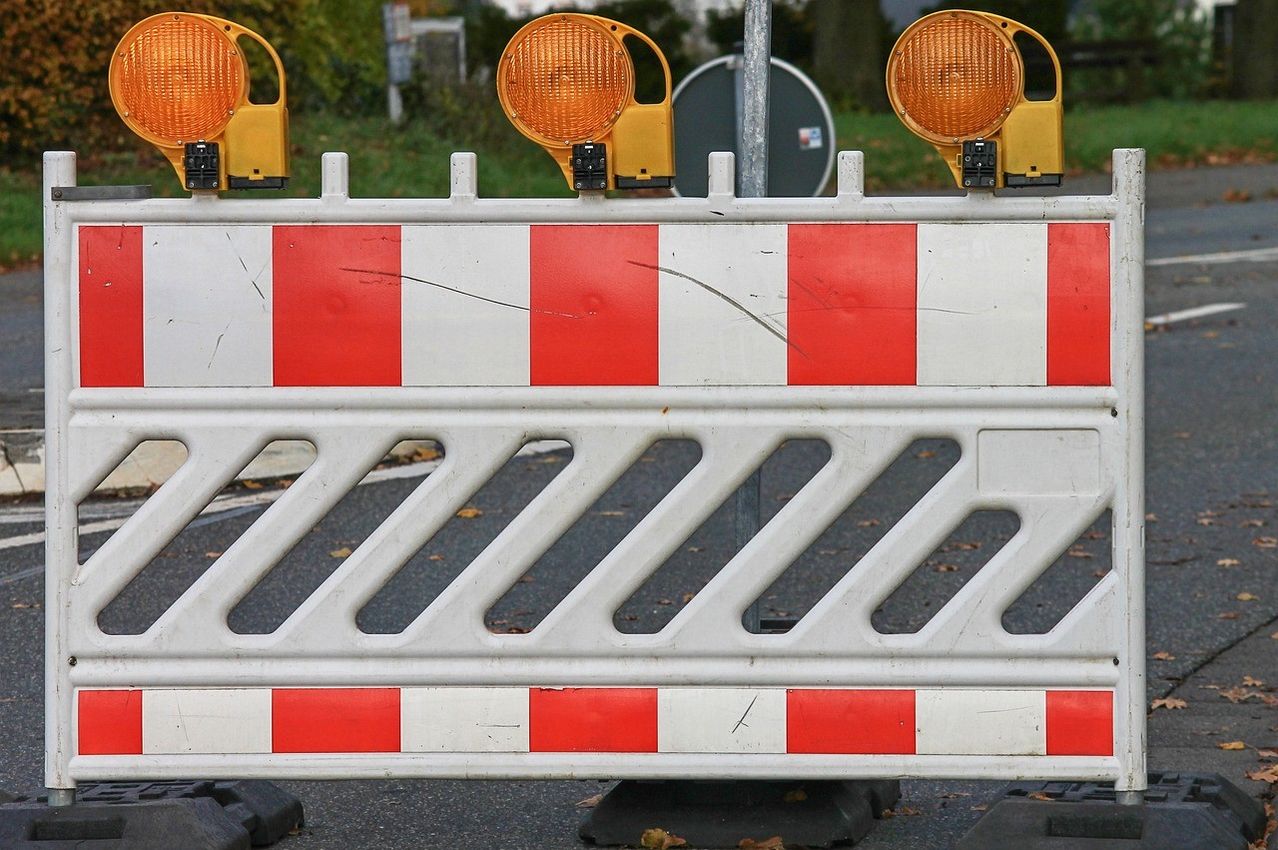 Ein Nahaufnahme einer Verkehrssperre mit abwechselnden roten und weißen Streifen. Oben sind vier orange reflektierende Warnleuchten angebracht.